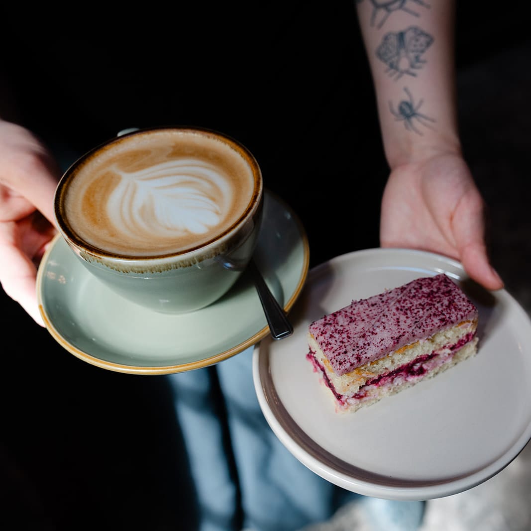 Blackberry and Mascarpone Traycake on a white plate being held next to a cappuccino