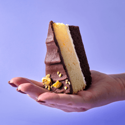 A slice of layered praline round cake standing on end in a hand with a purple background